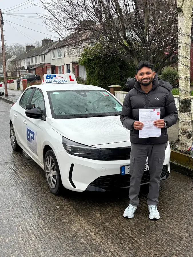 Student holding RSA driving test pass certificate next to BP Driving School white car