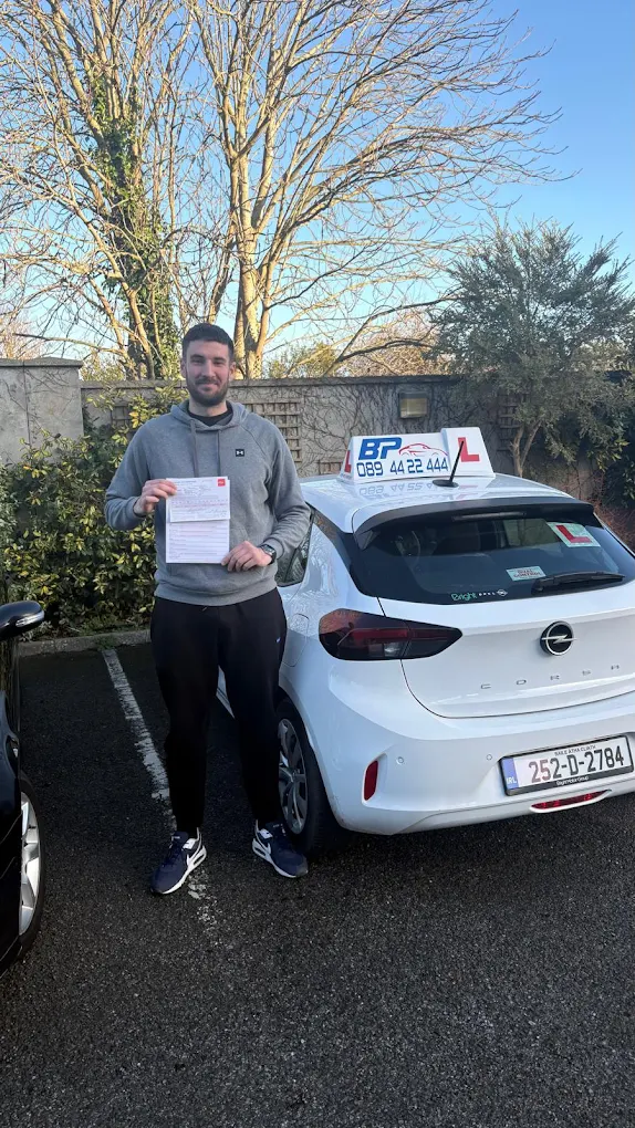 Student holding RSA driving test pass certificate next to BP Driving School Opel Corsa